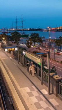Almanya 'nın Hamburg kentindeki Landungsbrucken istasyonuna ulaşan trenlerin hava gününden geceye geçiş zamanı. Metroya binen insanlar, Elbphilharmonie, liman ve marina ile panoramik manzara