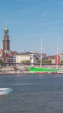 Elbe nehir kenarı ve Hamburg, Almanya 'daki St. Michaels kilise kulesinin panoramik zaman çizelgesi. İskeleye yakın teknelerle manzara, Jan Fedder gezinti güvertesi ve oradan geçen feribotlar. Nehir kenarındaki canlı şehir manzarası