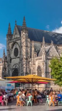 Bordeaux, Fransa 'daki Basilique Saint-Michel zaman çizelgesi, yüksek kulesi olan gotik bir simgedir. İnsanlar yakındaki kafeleri seviyor, yeşil ağaçların altında ve mavi bulutlu gökyüzü, şehrin canlı cazibesini yakalıyor.