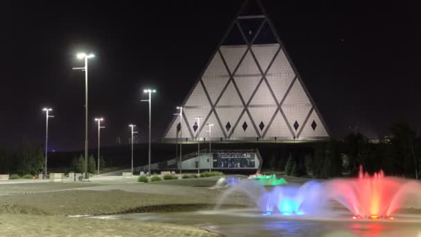 Place avec fontaine colorée la nuit près du Palais de la Paix et de la Réconciliation bâtiment intemporel hyperlapse à Astana, Kazakhstan . — Video