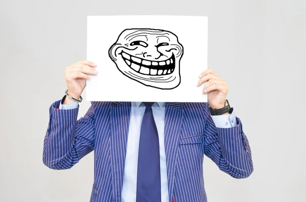Hombre de negocios hoding tarjeta con cara de troll sobre fondo gris — Foto de Stock