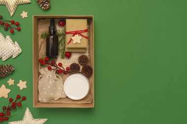 Yeşil arka planda organik kozmetik ürünleri olan mevcut kutu. Cam, ahşap süslemeler. Sıfır Noel konsepti. Düz görünüm yatar, alanı kopyala