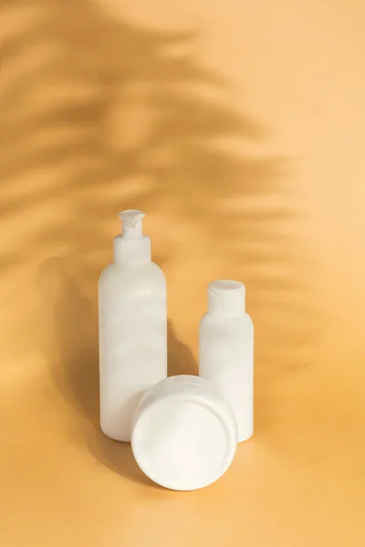 Kozmetik ürünler seti bej arka planda gölge eğreltiotu yaprakları ile taklit edilir. Dispenser şişesi, bir tüp krema. Damgalama, etiketleme ve paketleme.