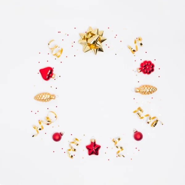 Kırmızı ve altın süslemelerden kare çerçeveli Noel kartpostalı, kurdele, konfeti ve beyaz arka planda ışıklar. Flay lay, üst görünüm, kopyalama alanı