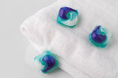 Çamaşır deterjanı ve arka planda temiz beyaz havlu olan birkaç çamaşır kapsülü..