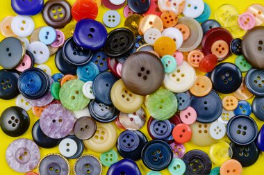 Sarı arka planda bir yığın renkli dikiş düğmesi. Terzilik konsepti. Düz yatıyordu.