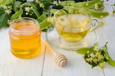 Kavanoz dolusu ıhlamur balı, bir fincan ıhlamur çayı ve dallı ahşap masa üzerinde ıhlamur çiçekleri..