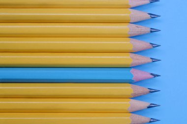 Sarı kalemler ve mavi arka planda bir mavi kalem. Üst Manzara. Farklılık kavramı.