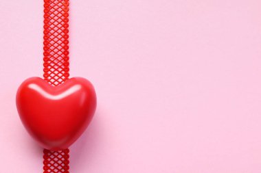 Kırmızı kalbin pembe arkaplandaki kırmızı kurdelenin üst görüntüsü, kopyalama alanı. Sevgililer Günü geçmişi. Aşk konsepti.