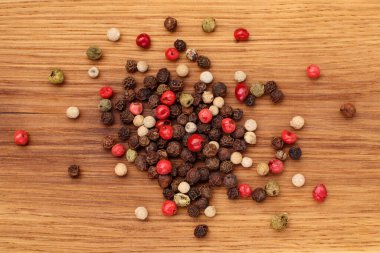 Ahşap tahtada çeşitli biber yığınları. Siyah, beyaz, yeşil ve kırmızı karabiber karışımı. Üst görünüm.