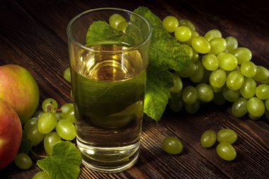 Bir demet yeşil üzümlü elma ve yeşil arka plandaki masada taze meyve suyu..
