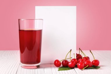 Bir bardak taze kiraz suyu, biraz taze kiraz ve kırmızı arka planda beyaz ahşap masa üzerinde boş kağıt çarşaf..