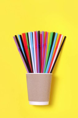 Sarı arka planda kağıt bardakta renkli kokteyl pipetleri.