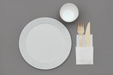 Beyaz kağıt tabağın üst görüntüsü, tahta çatal ve bıçak beyaz kağıt peçete üzerinde gri arka planda. Doğal malzemelerden çevre dostu tek kullanımlık sofra takımı..