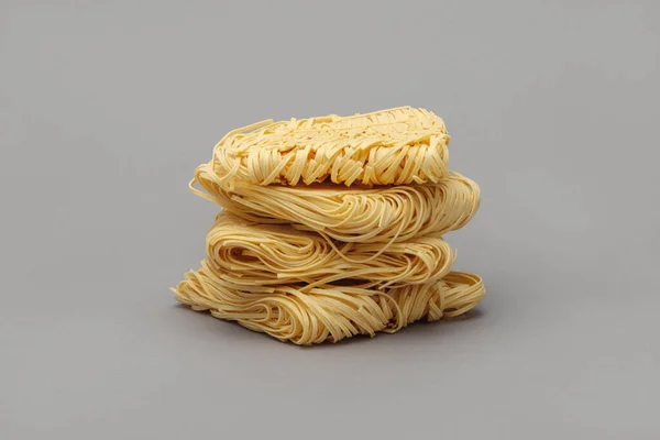 Gri arka planda bir yığın kuru yumurta eriştesi (makarna yuvaları).