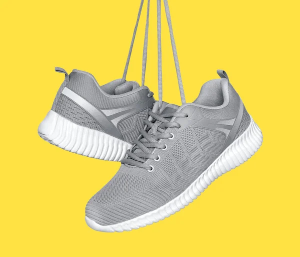 A pair of gray sneakers hanging on laces on a illuminating yellow background — Stock Photo, Image