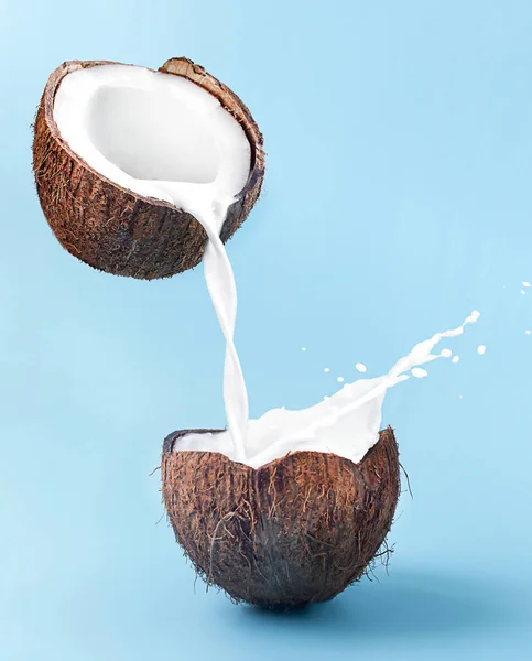 Melk gieten van kokosnoot in kokosnoot met plons op blauwe achtergrond — Stockfoto