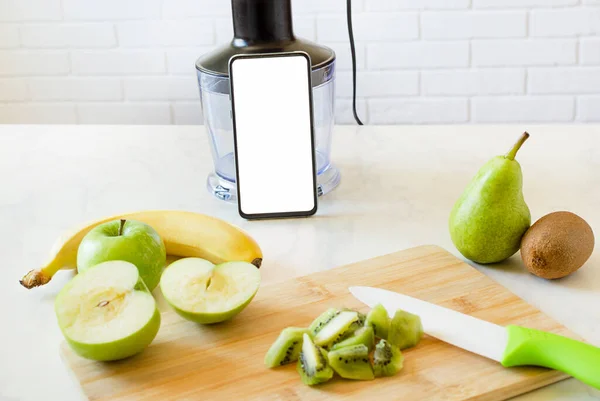 Karıştırıcıda smoothie yapmak için dilimlenmiş meyve ve tarifli bir telefon..