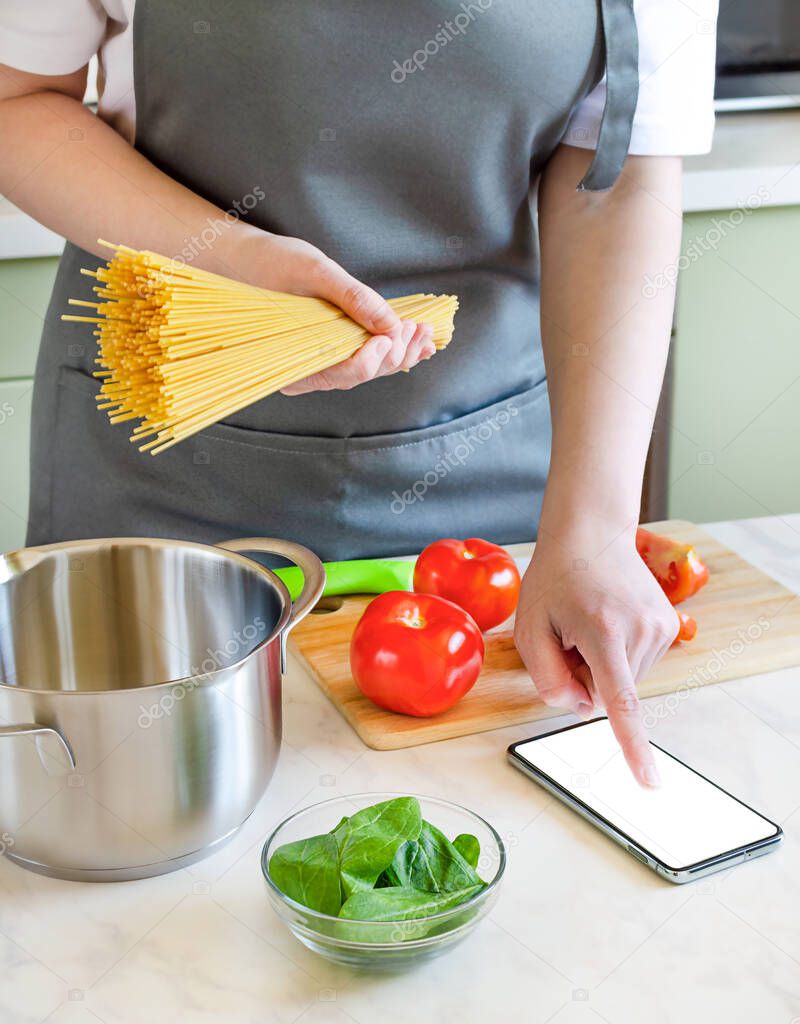 female hands preparing ingredients for pasta on a wooden board. cooking spaghetti with tomatoes and spinach at home using a recipe from the Internet.