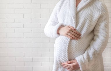 Bornozlu hamile bir kız elleriyle karnını okşuyor..