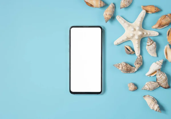 Summer holiday concept with phone, sea shells and starfish on light blue summer background with copy space.