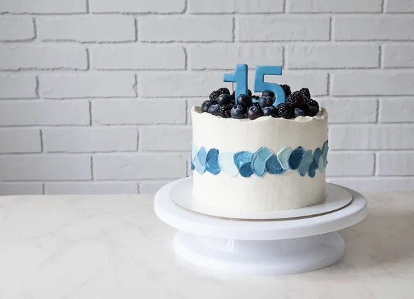 birthday cake with figures of 15 and blueberries and blackberries. cake with blue decor and a copy space.