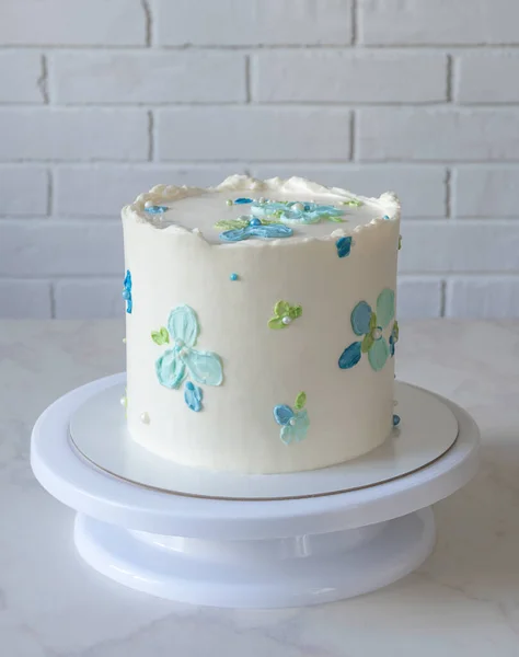 Uzun beyaz pasta, üzerinde krem rengi mavi çiçekler olan bir tezgahta. — Stok fotoğraf