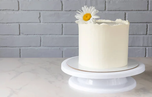 Torta bianca alta su uno stand con un arredamento di un fiore di camomilla — Foto Stock