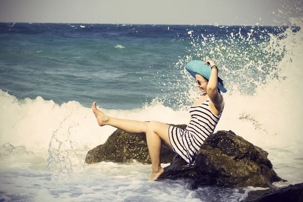 Hermosa mujer sentada en una piedra y salpicando en el mar. Estilo vintage —  Fotos de Stock