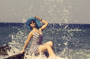 Bir taş üzerinde oturan ve denizde sıçramasına güzel kadın. Vintage tarzı