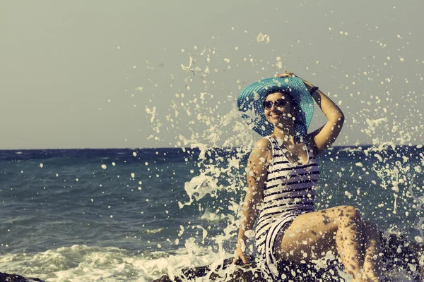 Hermosa mujer sentada en una piedra y salpicando en el mar. Estilo vintage — Foto de Stock