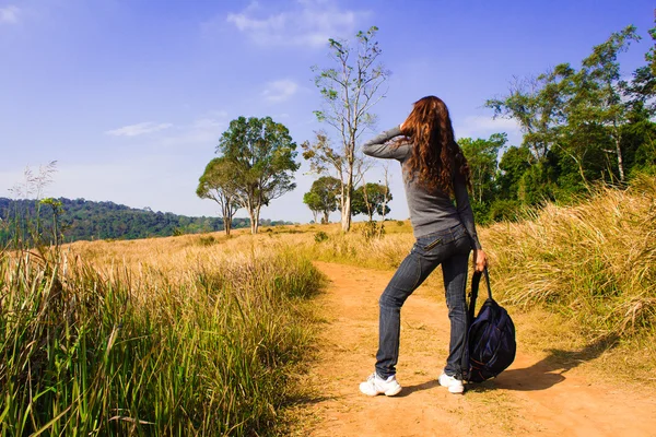 Egy fiatal nő hátizsákkal egy poros országúton sétál. — Stock Fotó