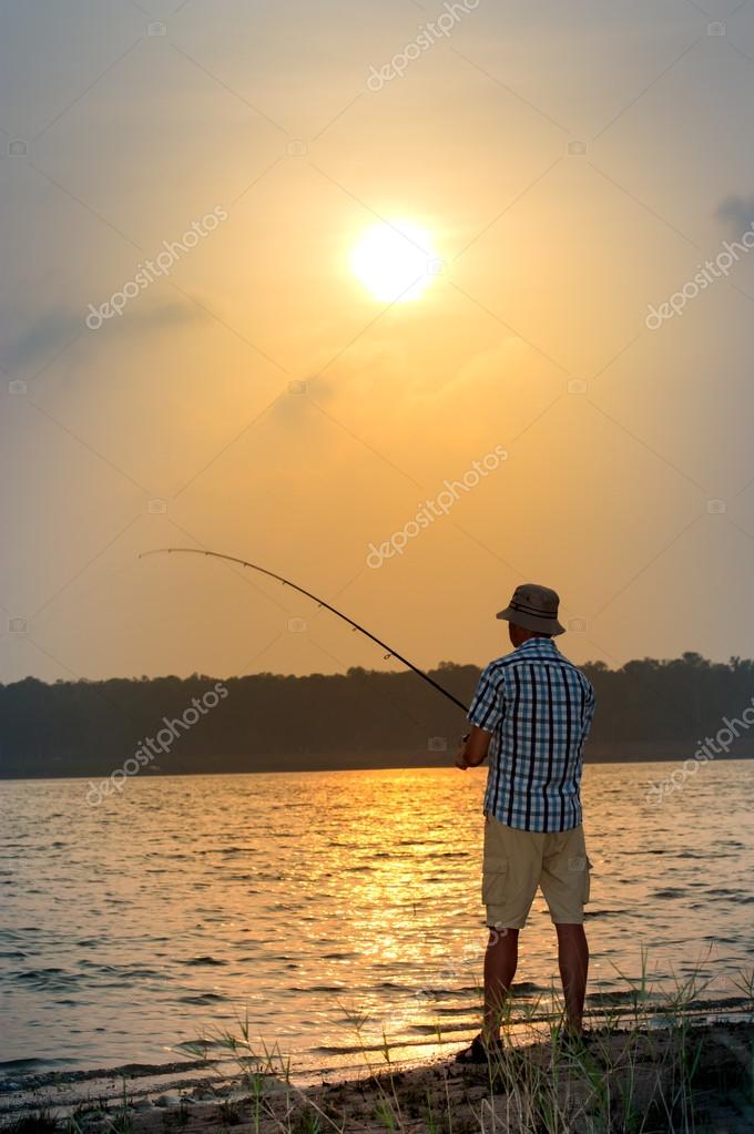 Young man fishing from a shore at sunset — Stock Photo © 2adrenalin@mail.ru  #63858769
