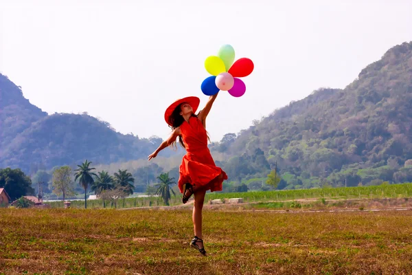 快乐的跳跃女人束五颜六色的气球在草地上 图库图片