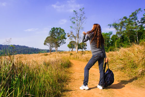 Young woman with backpack is walking on a dusty country road — Stock Photo, Image