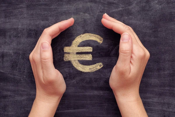 Hands protecting drawn euro sign on black chalkboard background — Stock Photo, Image