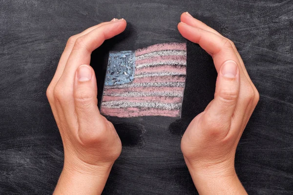 Manos protegiendo la bandera de EE.UU. dibujada sobre fondo de pizarra negro — Foto de Stock