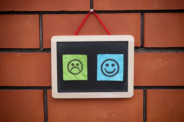 Two paper notes with happy and sad faces on blackboard — Stock Photo, Image