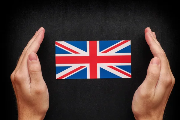 Hands protecting British Flag on black chalkboard background — Stock Photo, Image