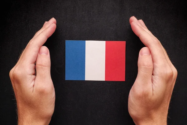 Manos protegiendo la bandera de Francia sobre fondo de pizarra negra —  Fotos de Stock