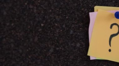 Üzerinde soru işareti olan bir sürü yapışkan not bir mantar tahtaya tutturulmuş. Kapat..