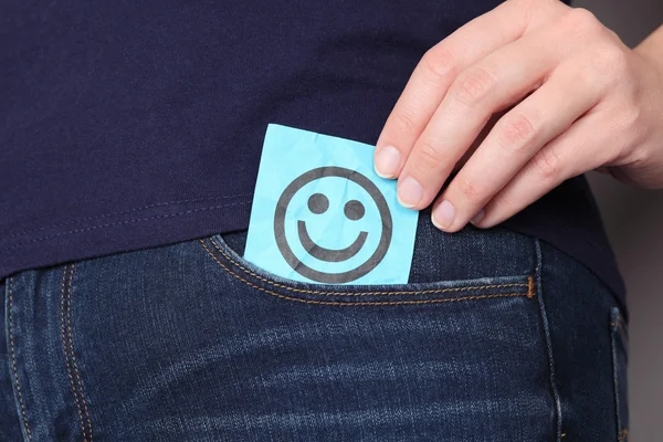 Бумажная записка с улыбающимся лицом в кармане джинсов — стоковое фото