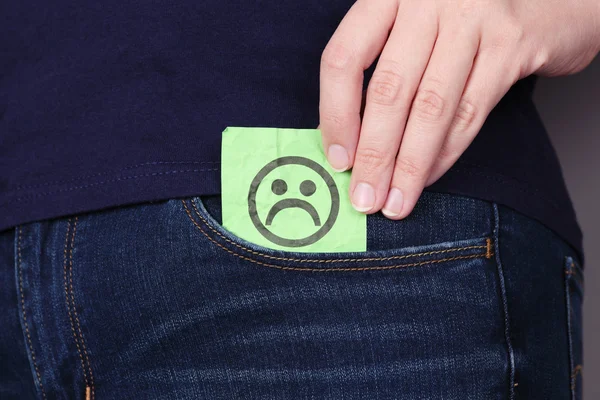 Nota di carta con la faccia triste in una tasca di jeans — Foto Stock