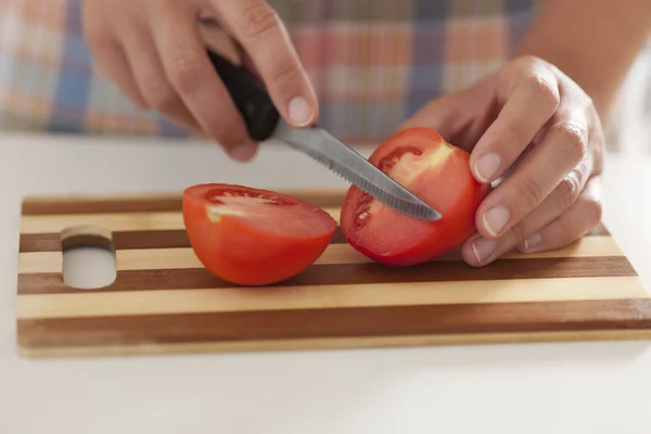 Woman cuts tomato on cutting board — Stock Photo, Image