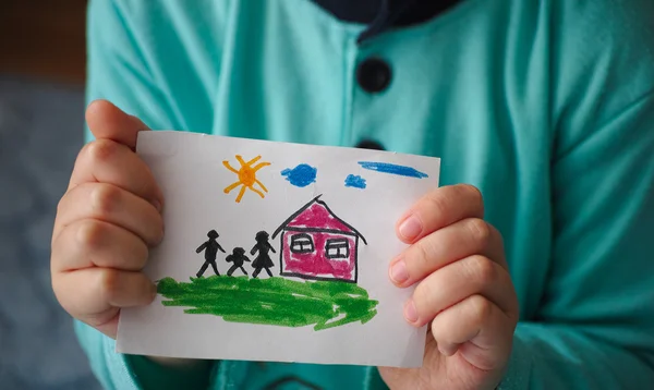 Ребенок держит нарисованный дом с семьей — стоковое фото