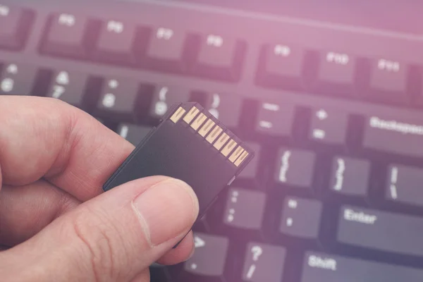 Hand holds SD Card against computer keyboard — Stock Photo, Image