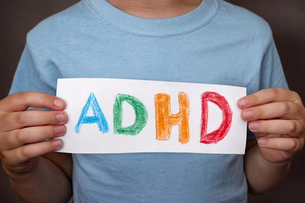 Il ragazzo tiene il testo dell'ADHD scritto su un foglio di carta Immagini Stock Royalty Free