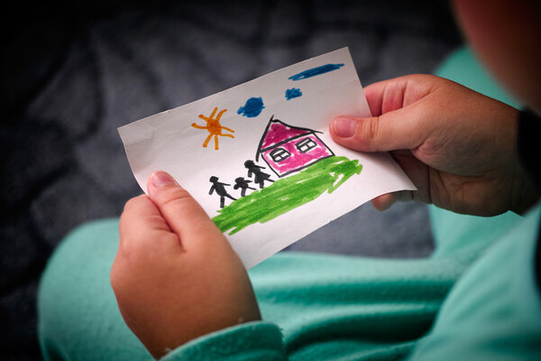 Child holds a drawn house with family