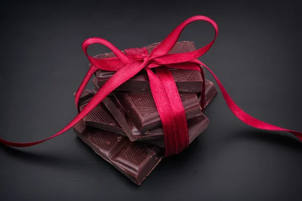 Chocolat noir avec ruban rouge sur fond noir — Photo