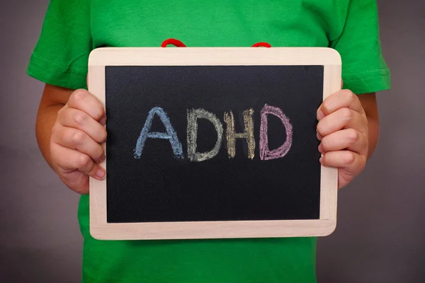 Young boy holds ADHD text written on blackboard — Stock Photo, Image